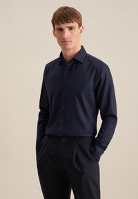 Camicia a maniche lunghe blu navy in tessuto morbido, con colletto classico e patta con bottoni, indossata con pantaloni eleganti scuri.