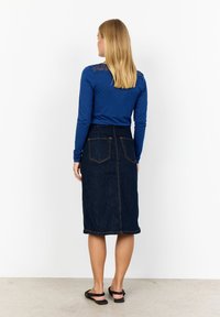 Blå långärmad topp med spetsdetaljer på axlarna, kombinerad med en mörk denim midi-kjol som har två bakfickor och kontrastsömmar.