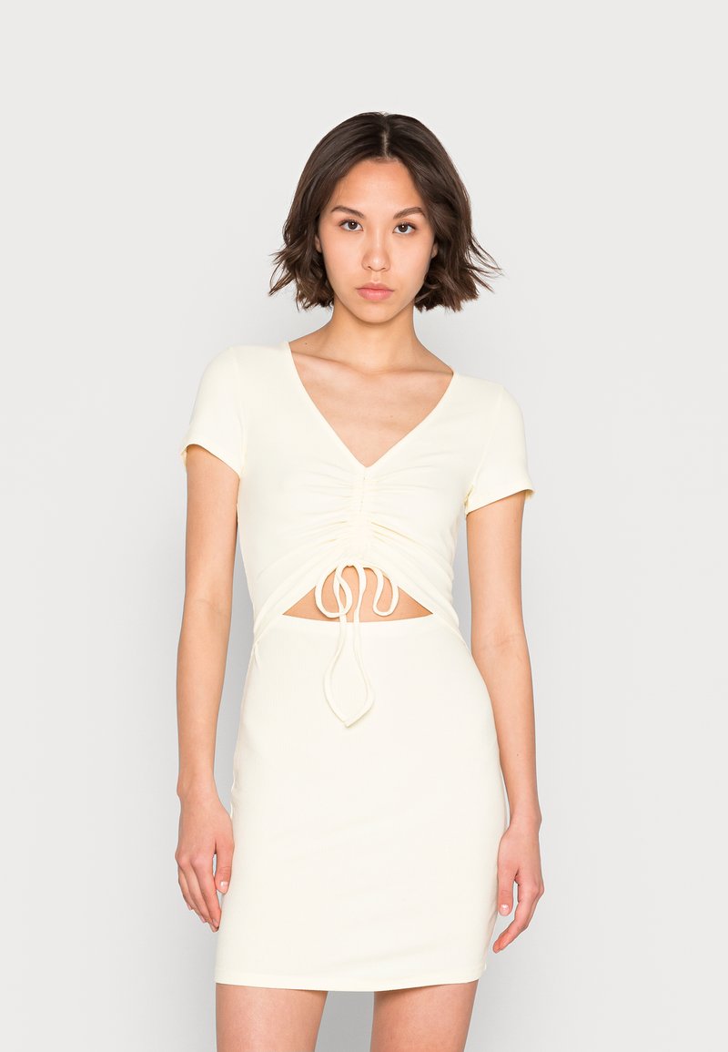 Vestido de tecido canelado em cor creme com um silhueta ajustada, mangas curtas, decote em V e detalhes frontais pregueados com fecho em laço.