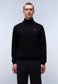 Zwarte coltrui van zacht materiaal met nauwsluitende manchetten. Bevat een klein logo op de borst en is gecombineerd met donkere broeken.