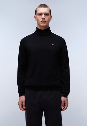 Suéter de cuello alto negro hecho de una tela suave con puños ajuste. Presenta un pequeño logo en el pecho, combinado con pantalones oscuros.