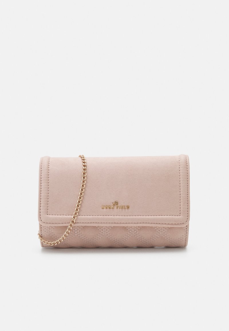 Pochette en daim rose avec bandoulière en chaîne dorée, design matelassé au bas et logo embossé. Elle présente une fermeture à rabat et une texture lisse.