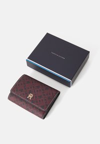Tommy Hilfiger wallet in dark red and black pattern with a gold logo. It has a textured finish and is presented in a navy blue box.