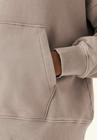 Sudadera beige con un bolsillo delantero, puños y dobladillo acanalados. Textura suave y diseño casual, ideal para el uso diario.