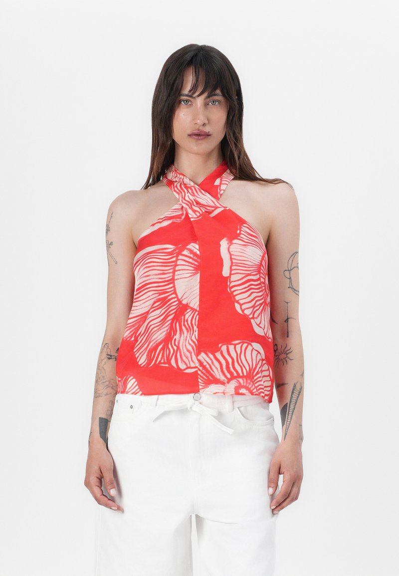 Red halter top with a floral pattern in white, featuring a crossover design at the neck. Worn with white high-waisted pants.