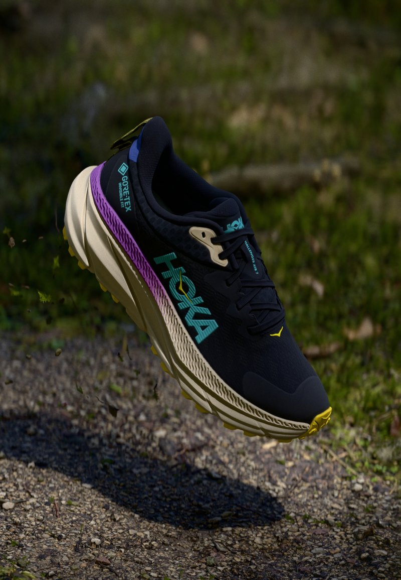 Chaussure de sport noire avec une tige texturée, ornée d'accents colorés en turquoise et violet, et dotée d'une semelle rembourrée de couleur crème.
