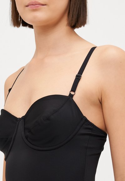 Schwarze Bademode mit strukturiertem, unterbrustunterstützendem Oberteil, verstellbaren Trägern und glatter Textur. Das Design umfasst einen abgerundeten Ausschnitt.
