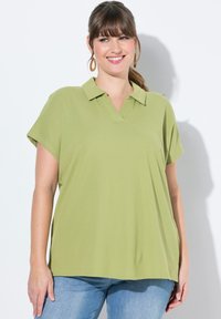 Polo shirt verde chiaro a maniche corte con colletto a V, realizzato in un tessuto teksturizzato, abbinato a jeans blu.