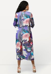Bunte Maxikleid mit langen Ärmeln, taillierter Taille und fließendem Stoff. Es hat Muster in Lila, Pink und Grün.