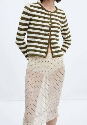 Femme portant un cardigan rayé vert et blanc boutonné avec une jupe beige transparente à pois noirs.