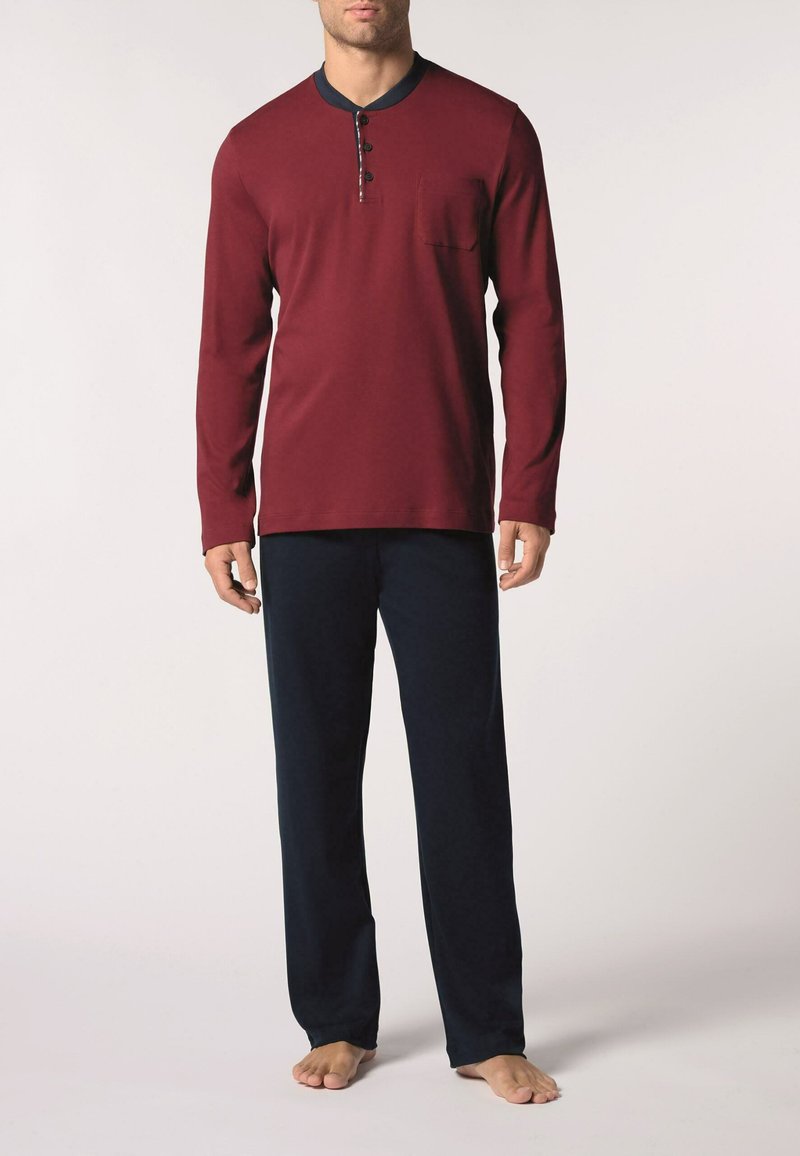 Completo da loungewear lungo color marrone con collo a giro, placca con tre bottoni e taschino sul petto; abbinato a pantaloni da pigiama blu navy.