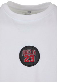 Balta kokvilnas t-krekls ar apaļu melnu uzlīmi ar sarkanu izšuvumu „BALLIN 23” uz krūtīm. Klasisks pamata apkakles dizains.
