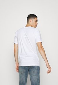 Weißes T-Shirt mit kurzen Ärmeln und Rundhalsausschnitt, aus weichem Stoff, präsentiert an einem Modell, das sich abwendet, kombiniert mit faded blauen Jeans.