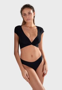 Crni bikini set s detaljem u obliku uvijenog čvora na vrhu s dubokim V izrezom i kratkim rukavima; donji dio s niskim strukom i glatkom završnom obradom.