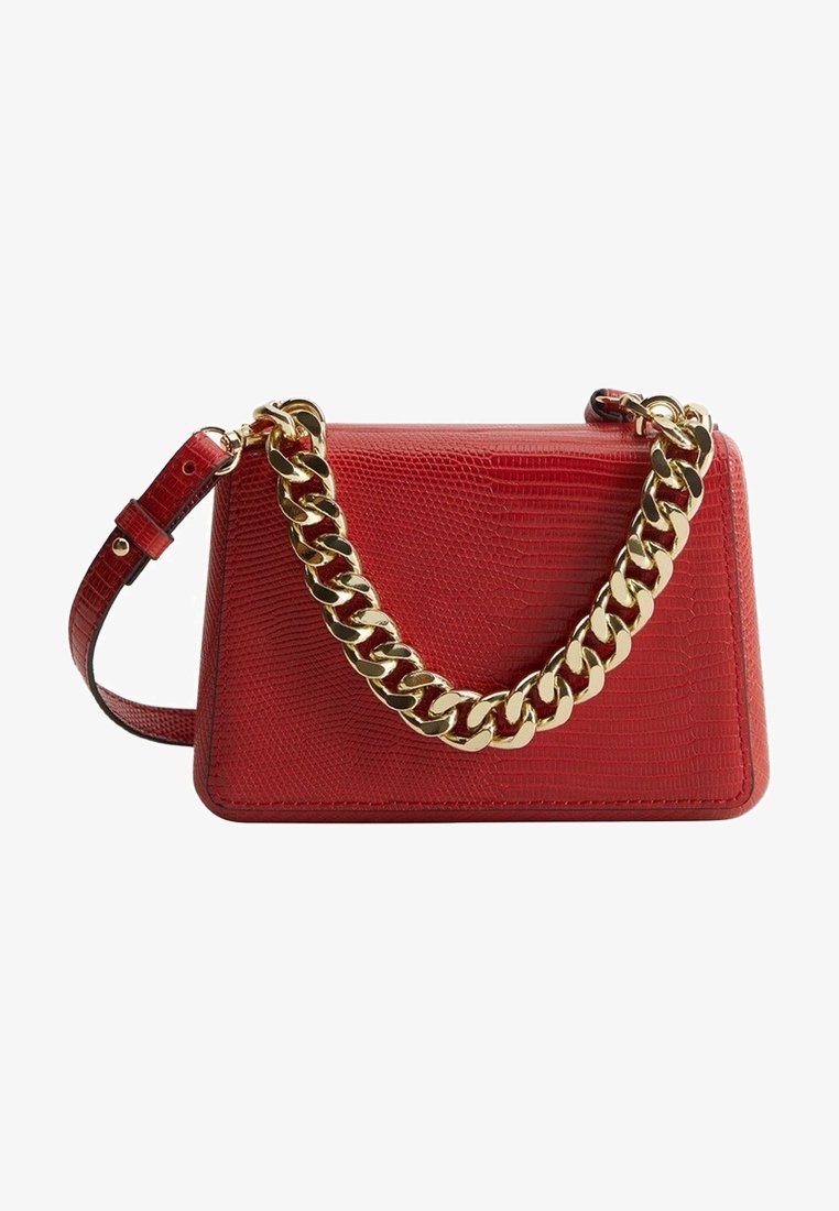 Sac à main rouge texturé avec une grande anse chaîne dorée et une bandoulière rouge réglable sur fond blanc.