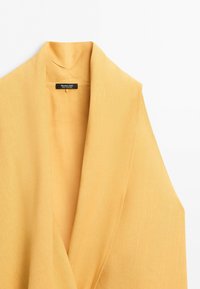 Yellow sleeveless blazer with wide lapels and visible label stitched inside collar on plain white background.