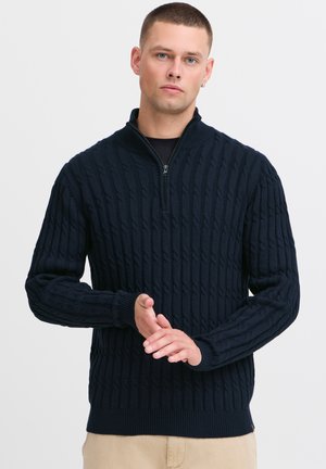Navy zip-neck sweater made of textured knit fabric, featuring a ribbed collar and cuffs, with a woven cable pattern throughout.