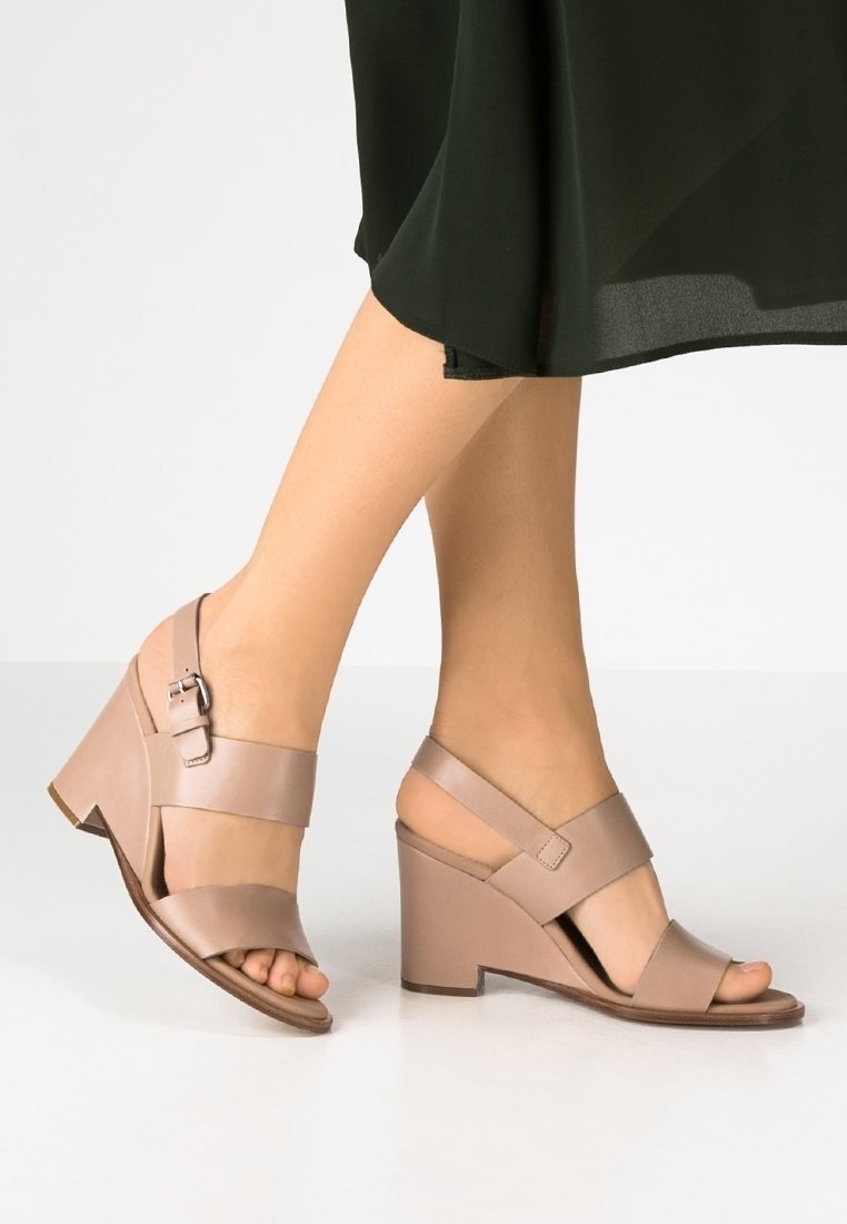 Sandales à talons hauts beiges avec de larges lanières croisées, boucle réglable à la cheville et design de talon en bloc solide. Texture en cuir lisse.