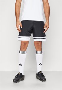 Sorte athletic shorts med hvide striber ved kanten, parret med knæhøje hvide sokker med sorte striber og sorte fodboldstøvler.