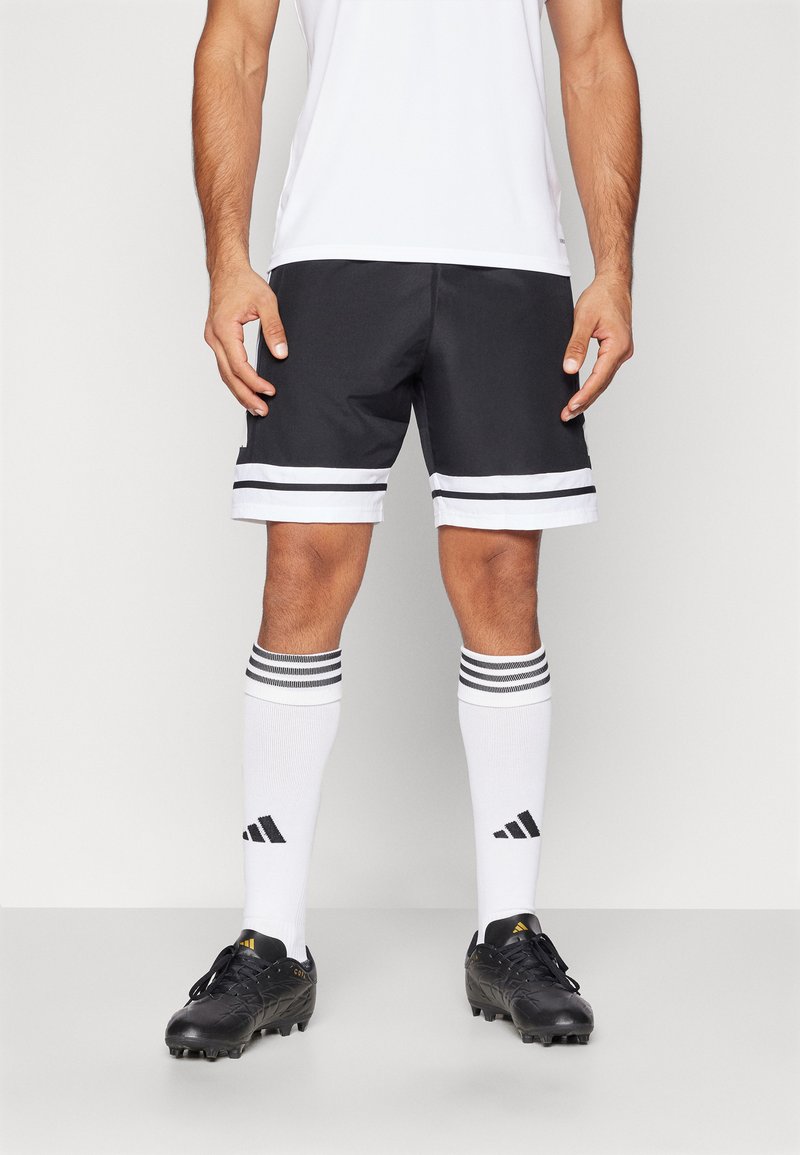 Svartidretter shorts med hvite striper på kanten, paret med knelange hvite sokker med svarte striper og svarte fotballsko.