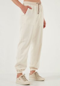 Beige joggingbroek gemaakt van zachte stof, met twee voorkruiden, een elastische tailleband met een trekkoord en elastische boorden bij de enkels.