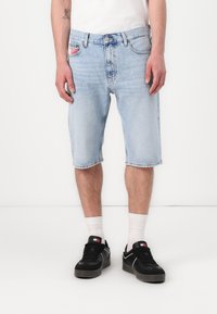 Light blue denim shorts with a regular fit, featuring a classic five-pocket design and slightly frayed hems. Worn with black sneakers.