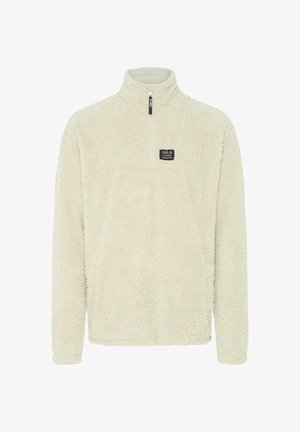 Kremfarget fleecegenser med høy krage, delvis glidelås og lite firkantet logo merke på brystet; har en myk, teksturert overflate.