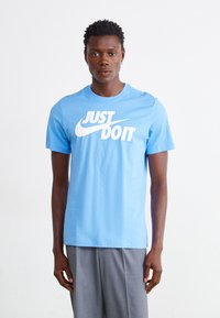 T-shirt de algodão azul claro com um grande texto branco "JUST DO IT" e um pequeno logótipo da Nike, com um clássico decote redondo e mangas curtas.