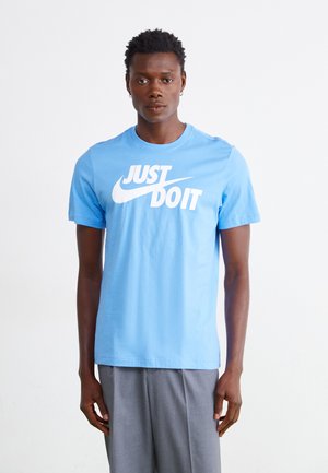 T-shirt in cotone azzurro chiaro con una grande scritta bianca "JUST DO IT" e un piccolo logo Nike, dotata di un classico collo rotondo e maniche corte.