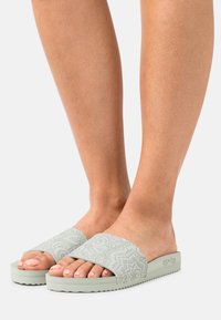 Light green slide sandals with a textured floral pattern on the strap and a patterned rubber sole. Lightweight and open-toe design.