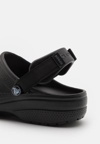 Black Crocs sandal featuring a textured upper, adjustable strap, and a thick sole with small circular perforations for breathability.