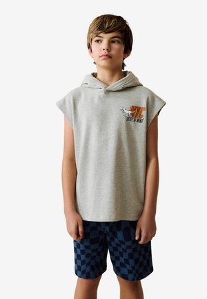 Grijze mouwloze hoodie met een voorzak en grafische print. Gepaard met donkerblauwe ruitjesshorts van zachte stof.
