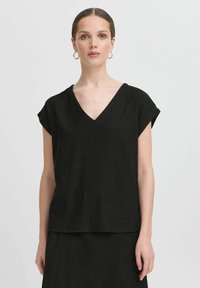 Top corto in lino nero con scollatura a V profonda, vestibilità ampia e design rilassato. Texture liscia e dettagli di cucitura minimi.