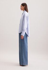 Camicia oversize a righe blu chiaro con maniche lunghe e polsini a bottone, abbinata a una gonna in denim chiaro a vita alta e taglio dritto.