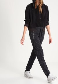 Felpa nera corta con lacci e tasche con zip, abbinata a pantaloni jogger grigi melangiati con fit affusolato e polsini alla caviglia. Sneakers bianche.