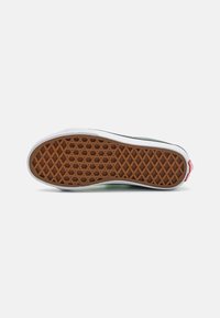 Suela de zapato de goma con un patrón de panal, que presenta una base marrón y bordes laterales blancos. Acento de etiqueta roja en el talón.