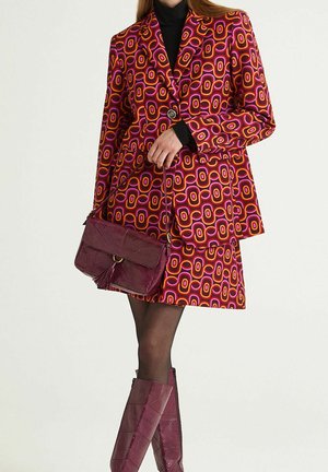 Ensemble blazer et jupe à motifs géométriques en rose, orange et violet, associé à un sac à main texturé bordeaux et des bottes assorties mi-hautes.