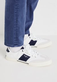 Zapatillas blancas con acentos en azul marino, que presentan una combinación de materiales lisos y texturizados, puntera redondeada y diseño con cordones.