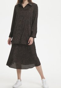 Brun leopardmönstrad långärmad skjorta med knappstängning, matchad med en koordinerad kjol. Modellen har på sig vita sneakers.