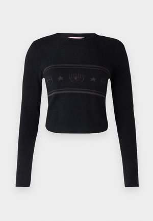 Juodas trumpas megztinis su ilgomis rankovėmis, turintis akcentuotą horizontalią juostą su stilizuotais raštais ir žvaigždėmis per krūtinę.