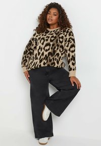 Leopardmönstrad stickad tröja i beige och mörkgrön, med rund hals och ribbade muddar, som bärs med svarta vida jeans och vita sneakers.