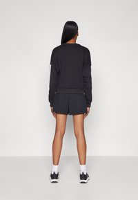 Svart sweatshirt med rund halsringning och ribbade ärmslut, kombinerad med mörka shorts. Stylad med atletiska sneakers och vita strumpor.