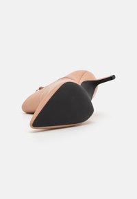 Zapato de tacón alto nude con parte superior de cuero liso y punta afilada, con una suela de goma negra y un tacón de stilettos delgado.