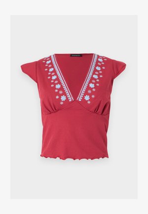 Blouse rouge à manches courtes avec un col en V profond, broderie florale blanche le long de l'encolure, et détails froncés sous la poitrine.
