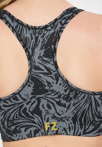 Svart och grå sportbehå med ett virvlande mönster, som har en racerback-design. Framsidan har en framträdande gul "FZ"-logotyp.