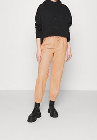 Schwarzer Kapuzenpullover, pfirsichfarbene Jogginghose aus Kunstleder mit elastischen Bündchen, kombiniert mit schwarzen schnürbaren Chunky-Stiefeln. Einfaches Design, lockere Passform.