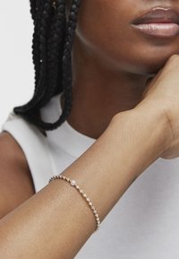 Bracciale in oro e perle su un polso, con delicate perle rotonde e una superficie liscia, che si abbina al tono della pelle. Design semplice.