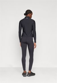 Top sportivo nero con colletto alto e maniche lunghe, abbinato a leggings neri aderenti. Entrambi i capi presentano una texture liscia.