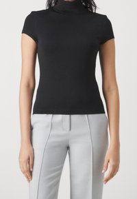 Černý krátký rolák s krátkými rukávy z hladké, elastické látky; doplněný světle šedými elegantními kalhotami s výraznými záhyby.