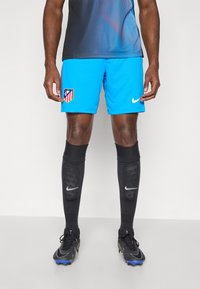 Fodboldshorts i lys blå med et klubemblem, parret med sorte knæhøje sokker med et hvidt Nike-logo og sorte fodboldstøvler.